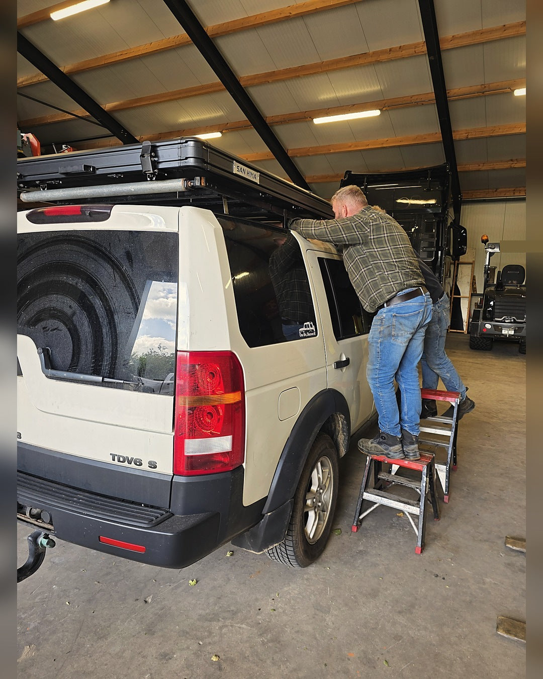 Hardshell daktent wordt op het dakrek van een Land Rover Discovery gezet in de werkplaats