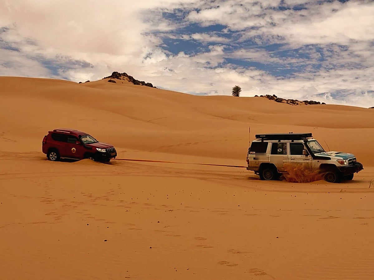 Two Land Cruisers in the dunes, one pulling the other free with a kinetic recovery rope