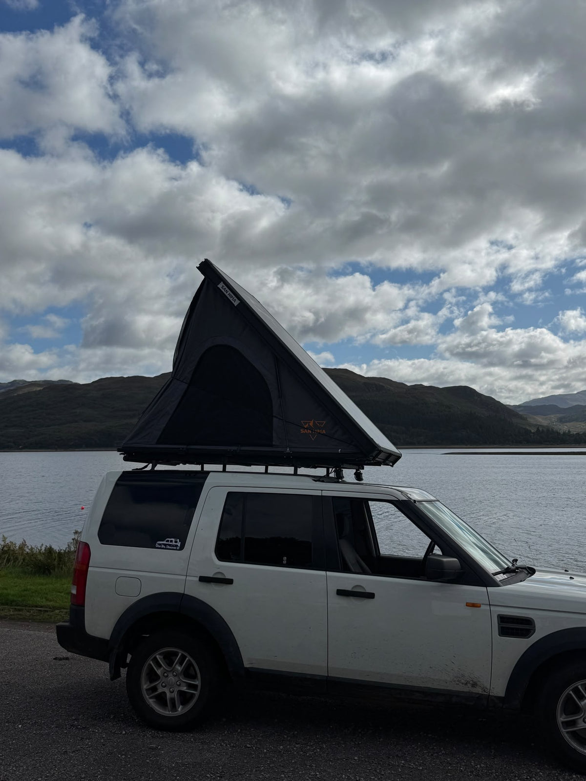 Land Rover Discovery van een klant met opengeklapte LCM hardshell daktent aan een meer in de bergen