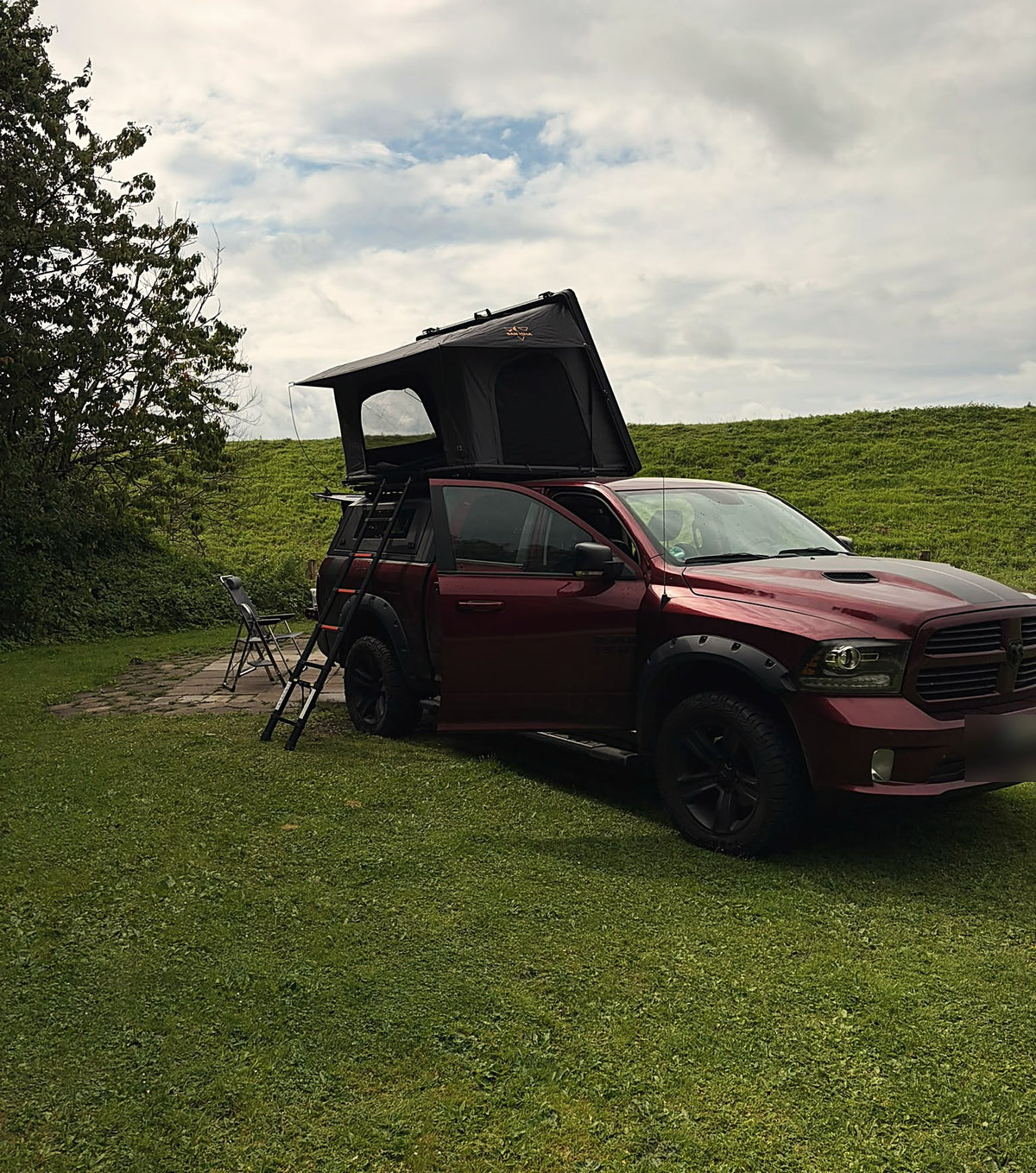 RAM 1500 pick-up met canopy van een klant, LCM Oasis hardshell daktent opengeklapt op een camping aan de dijk