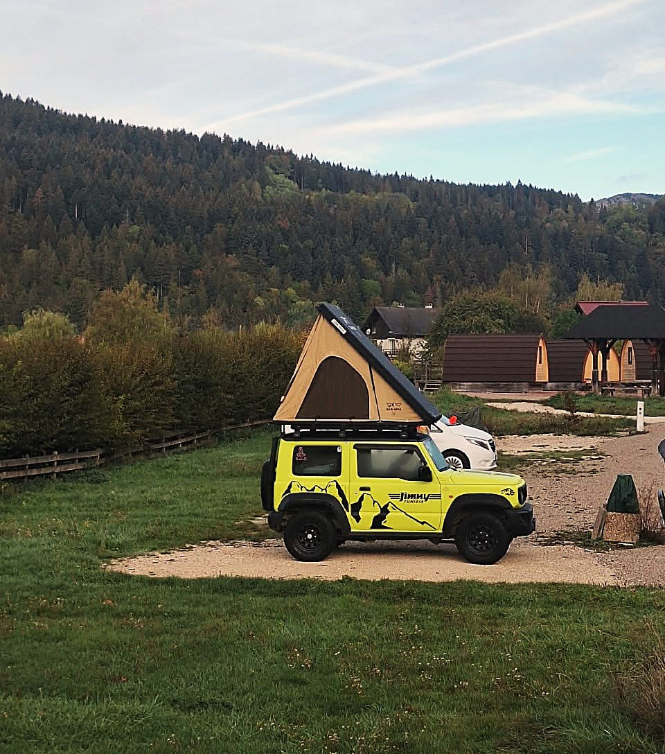 Suzuki Jimny van een klant uit Tunesië met opengeklapte LCM hardshell daktent op een camping aan de bosrand