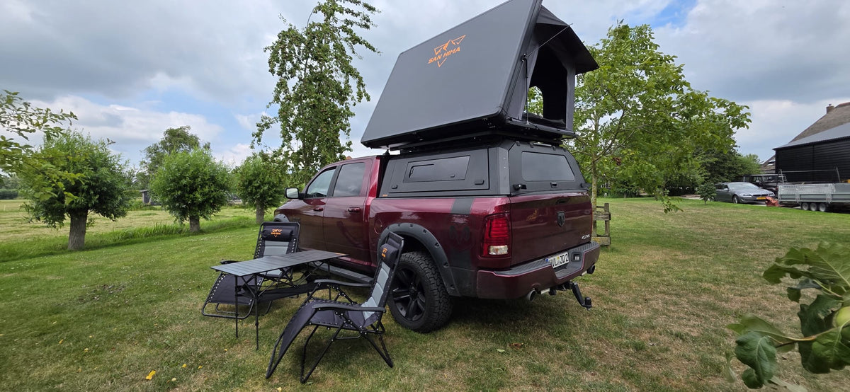 RAM pick-up with LCM Offroad Oasis hardshell rooftop tent, camping chairs and aluminium camping table on the grass