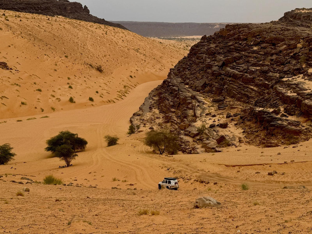 Land Cruiser on a sand track between black rocks in the Sahara